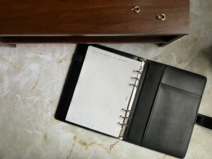 A lined notes page inside a planner with a motivational quote handwritten at the top, enclosed in a sleek black leather binder.